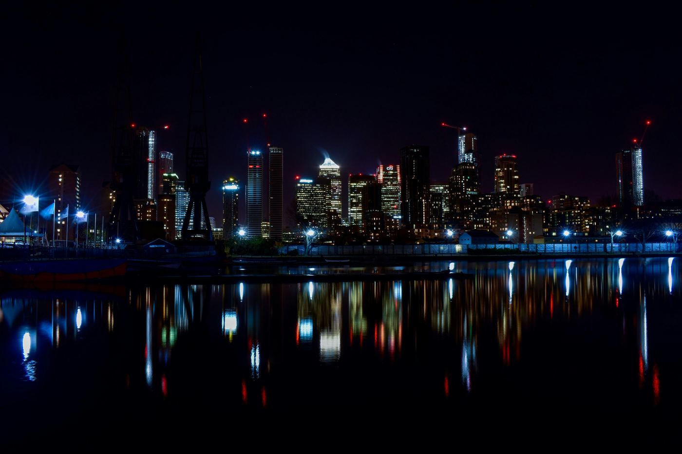 The Canary Wharf skyline at night, reflected in the water of the London Docklands.